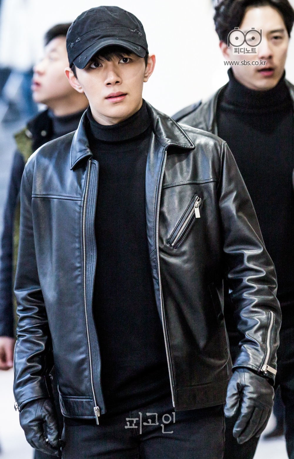 무표정으로 정면을 응시하며 걸어가는 오승훈. 뒤에는 검은색 옷을 입은 부하들