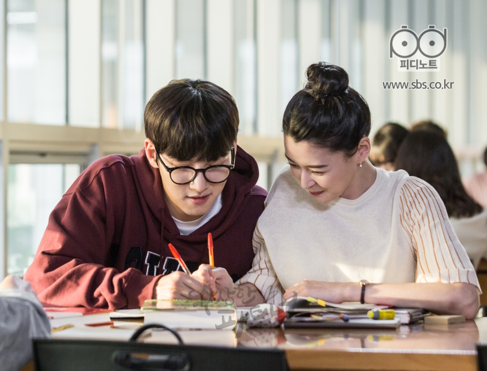 지욱과 유정이 대학교 도서관에서 나란히 앉아 공책에 함께 낙서하는 정면의 모습.