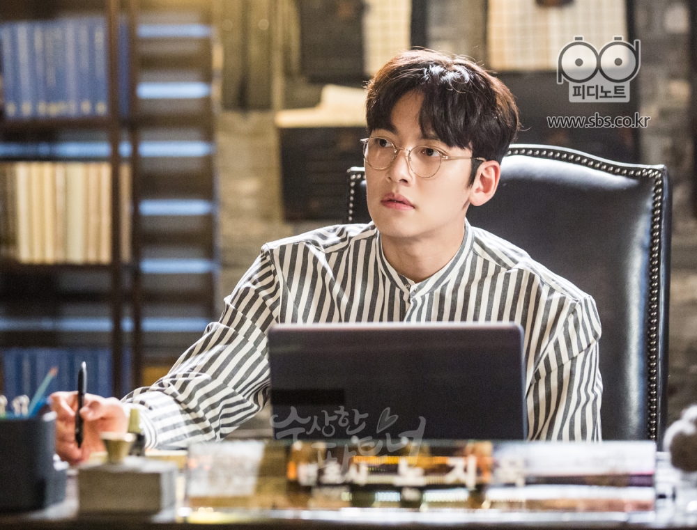 스카프를 두른 봉희가 나가자 신경 쓰이는 지욱. 책상에 앉아서 봉희가 나가는 곳을 보고 있다.